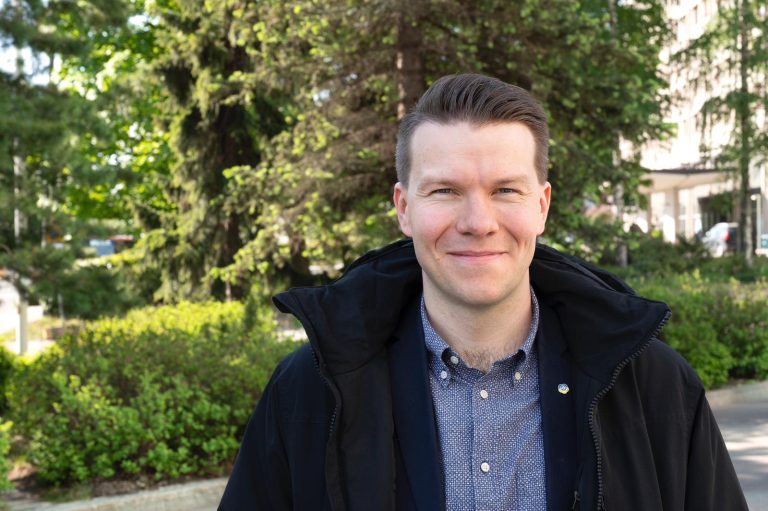 Kuvan etuosassa seisoo Mikkel Näkkäläjärvi katsoen suoraan kameraan. Taustalla näkyy kesäisiä lehtipuita.